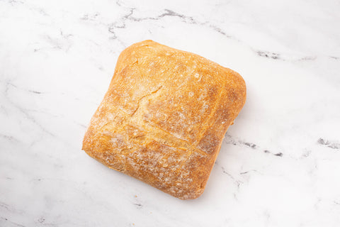 A rustic square loaf of bread with a golden-brown crust and a light dusting of flour, placed on a white marble surface.