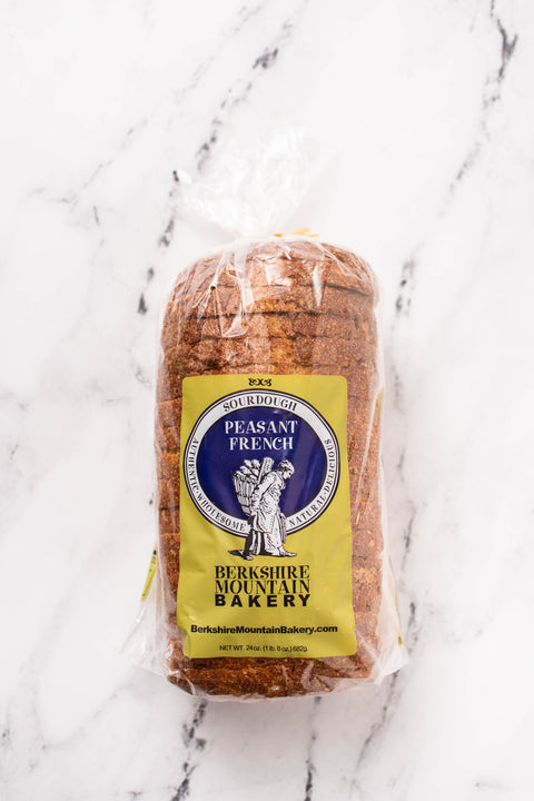 A loaf of packaged Peasant French bread from Berkshire Mountain Bakery, wrapped in clear plastic with a yellow and blue label, set on a white marble surface.