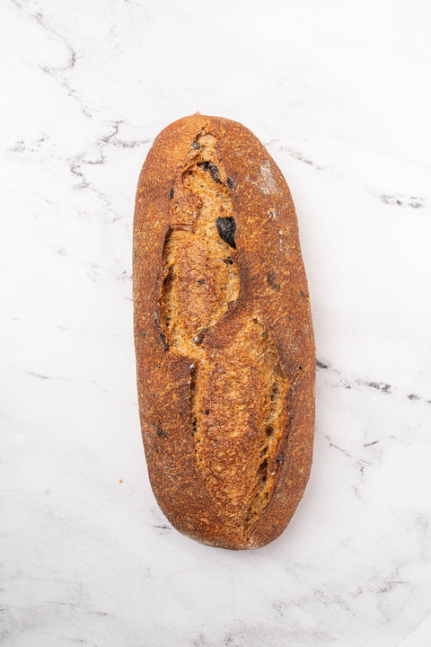 An artisanal sourdough raisin bread loaf with a golden-brown crust and dark charred scoring, placed on a white marble surface.