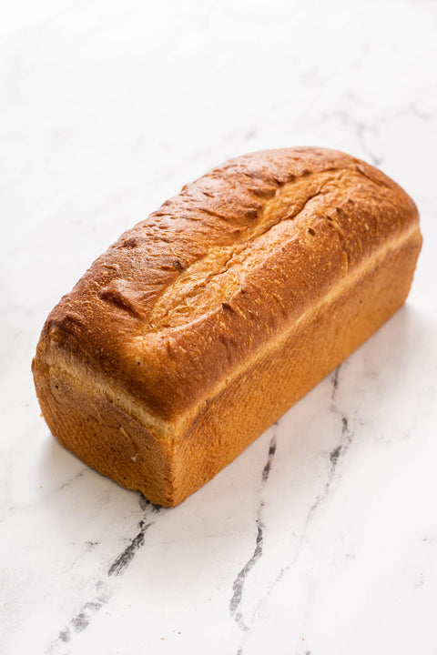 A freshly baked San Francisco style pan loaf of golden-brown bread resting on a white marble surface.