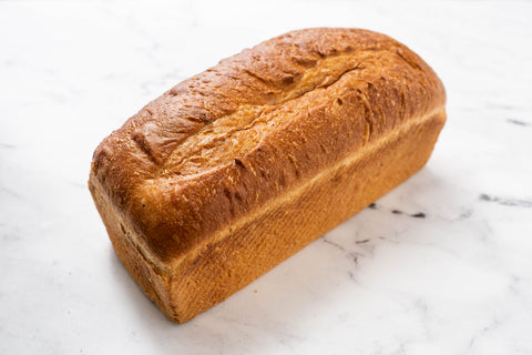 A freshly baked San Francisco style pan loaf of golden-brown bread on a white marble surface.