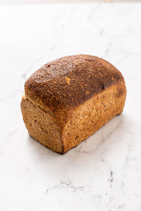A single loaf of rustic spelt bread sits on a white marble surface with subtle gray veining.