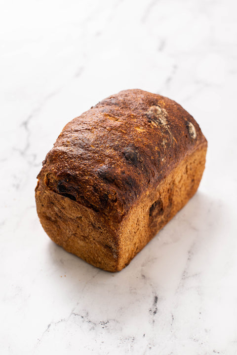 A single loaf of rustic spelt raisin bread with a dark toasted crust, photographed on a white marble surface.