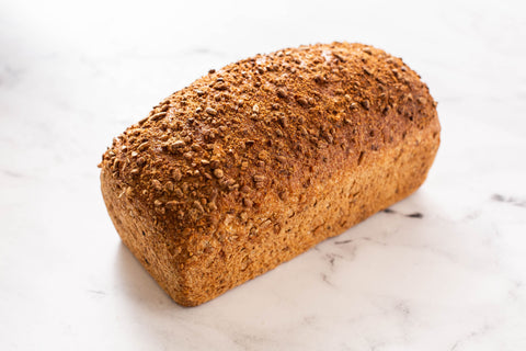 A single loaf of rustic whole wheat bread with a textured, flax seed-dusted crust, resting on a white marble surface.