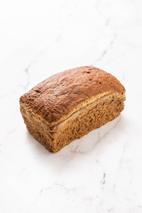 A single loaf of brown bread, likely banana bread or a similar sweet bread, photographed on a white marble surface.