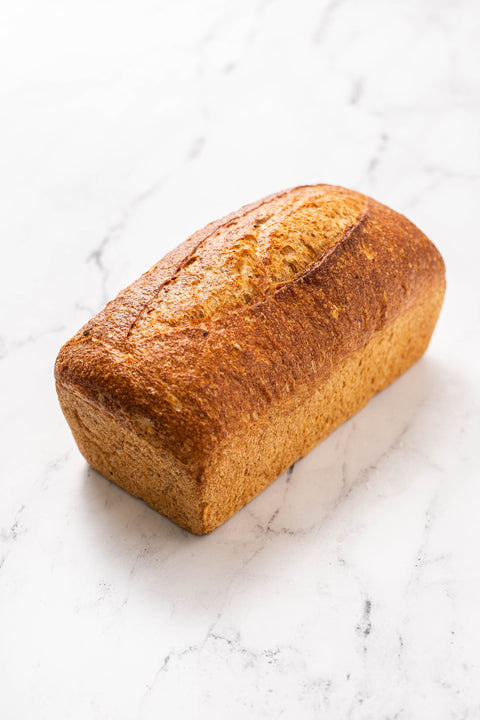 A single loaf of rustic artisan bread with a golden-brown crust, photographed on a white marble surface.