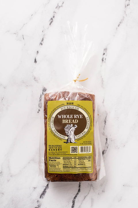 A loaf of Whole Rye Bread in a clear packaging with a yellow and brown label, placed on a white marble surface.