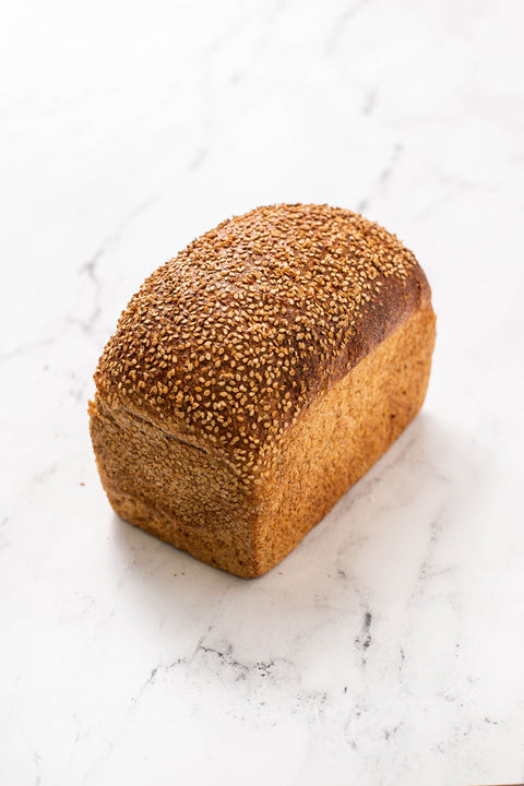 Whole wheat pan loaf of bread with a golden brown bake and sesame seed topping on a marble countertop